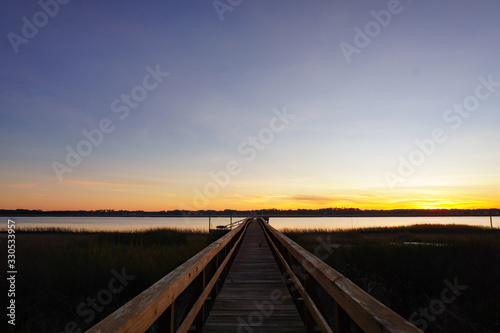 A long dock leads out to a marsh and river at sunset in South Carolina  copy space