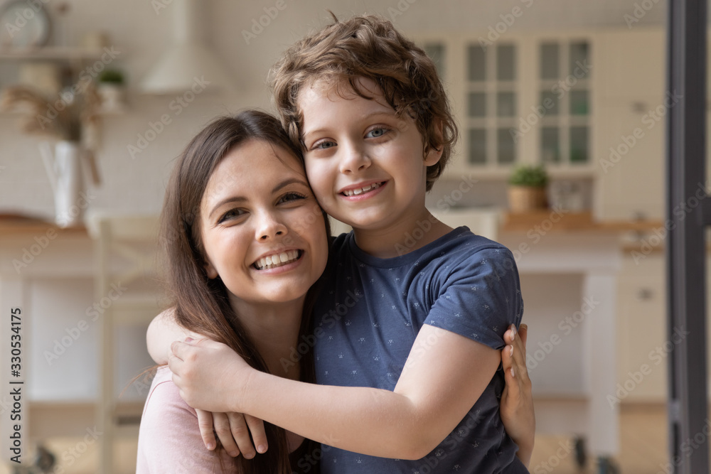 Close up portrait of smiling young mom and little preschooler son embrace look at camera posing at home, happy mother parent hug cuddle small boy child showing love and care relaxing together indoors Close up portrait of smiling young mom and little preschooler son embrace look at camera posing at home, happy mother parent hug cuddle small boy child showing love and care relaxing together indoors