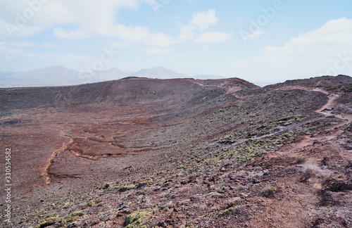 Der Vulkan Montana Roja de Playa Blanca mit einer Höhe von 194m und im Hintergrund die Südwestspitze der Atlantikküste auf der Kanareninsel Lanzarote