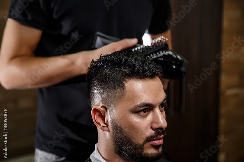 the guy is a dark-haired Asian Indian appearance on a haircut in a barbershop . cinematic image