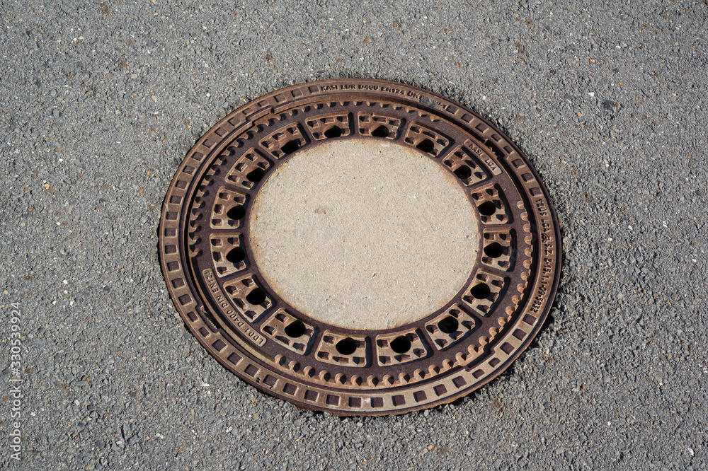 Manhole and utility hole in the asphalt surface. Rounded cover made of steel and metal is rusty. Manhole and utility hole in the asphalt surface. Rounded cover made of steel and metal is rusty.