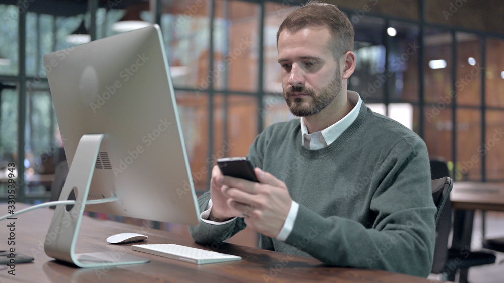 Young Man using Smartphone while sitting on Office Desk Young Man using Smartphone while sitting on Office Desk