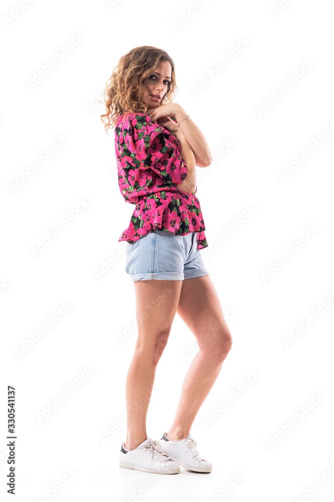Naklejka premium Side view of curly hair young hipster girl in floral shirt and jeans summer shorts posing. Full body length isolated on white background.
