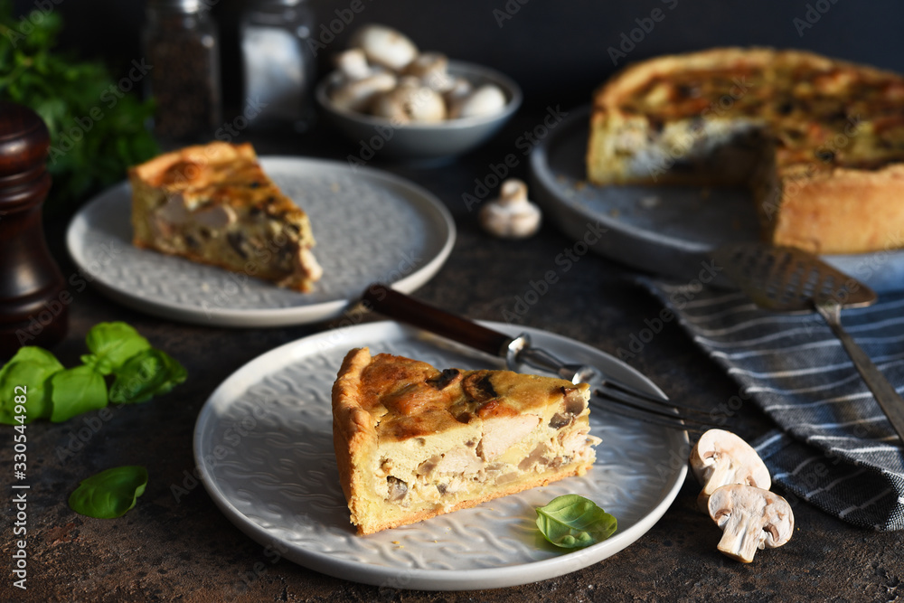 Tart slice on the kitchen table. Traditional quiche with chicken, mushrooms and cheese on a dark concrete background.