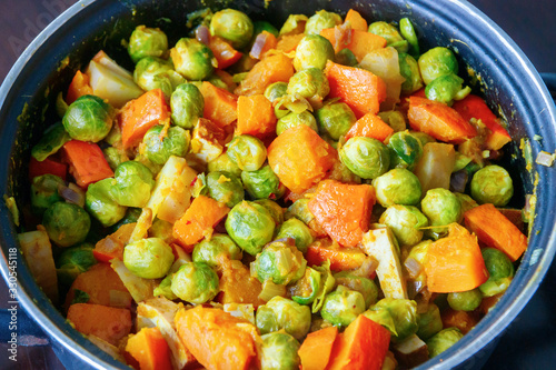Pan with a mix of cooked vegetables. Delicious meal with Brussels sprouts, pumpkin, onion, potato and tofu. Black background.