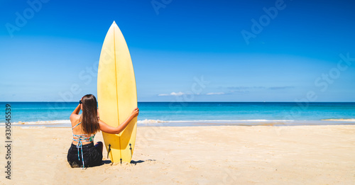 Women Caucasian hold a yellow surfboard on the beach. Women are viewing waves to surf the waves in good weather and clear skies during the summer in holiday and activity concept with copy space.