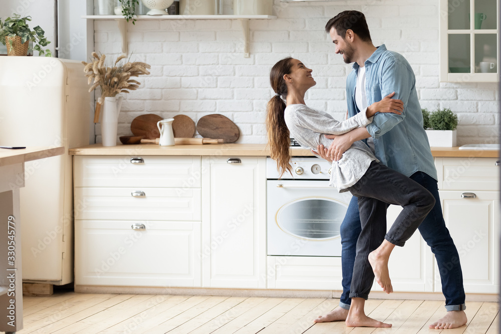 Happy loving young couple dancing romantic dance on date in modern kitchen, smiling husband and wife celebrating anniversary, enjoying tender moment, having fun, moving to music at home Happy loving young couple dancing romantic dance on date in modern kitchen, smiling husband and wife celebrating anniversary, enjoying tender moment, having fun, moving to music at home