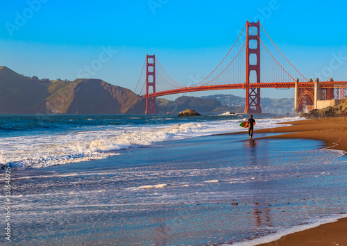 Unidentified surfer at sunset at Baker Beach by the famous Golden Gate Bridge, San Francisco, California, USA