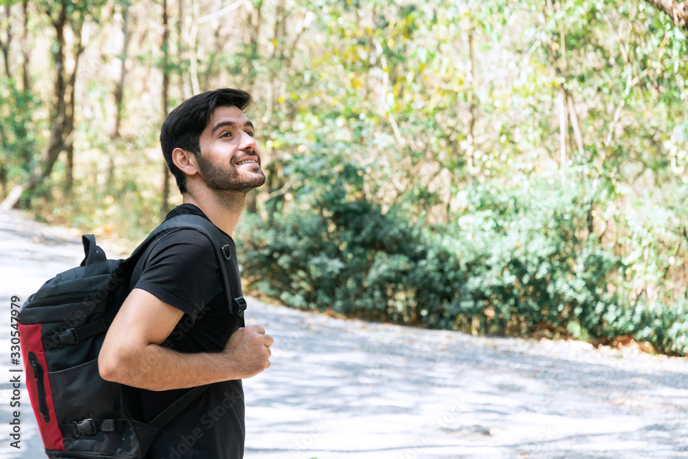 Closeup of cheerful young caucasian man in black t-shirt with backpack standing and looking to forest at National Park. Trekking and hiking travel concent. Closeup of cheerful young caucasian man in black t-shirt with backpack standing and looking to forest at National Park. Trekking and hiking travel concent.