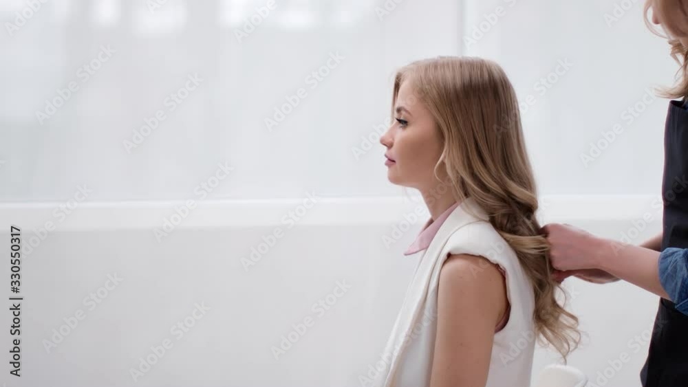 Female stylist strolling curly long blonde hair of young female model. Medium shot on RED camera Female stylist strolling curly long blonde hair of young female model. Medium shot on RED camera