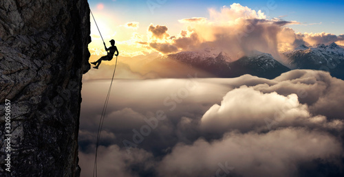 Silhouette Rappelling from Cliff. Beautiful aerial view of the mountains during a colorful and vibrant sunset or sunrise. Landscape taken in British Columbia, Canada. composite. Concept: Adventure