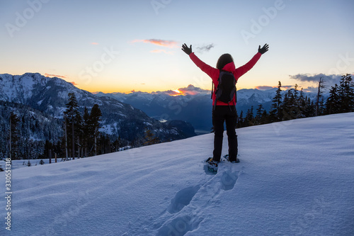 Adventurous Girl Snowshoeing in the snow on top of a mountain during a vibrant and colorful winter sunset. Taken on Anif Peak, Squamish, British Columbia, Canada. Concept: explore, adventure