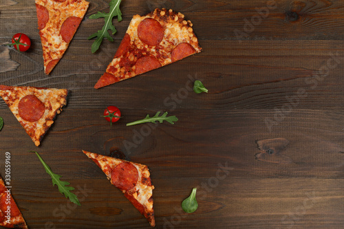 pieces of pizza with salami and tomatoes cherry on brown wood table