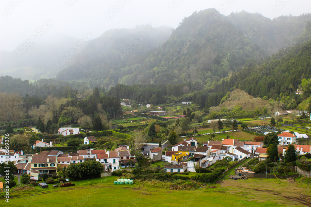 Foggy mountain valley landscape with village surrounded by lush green rainforest