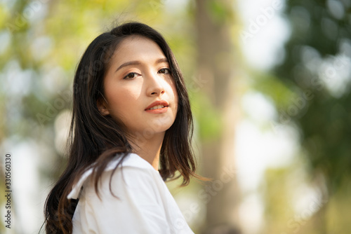 Portrait of young Asian woman wearing the white shirt in casual style smiling and enjoy life in the natural sunlight in the park, Relaxing moment, enjoying the nature, mindful and feel the fresh are.