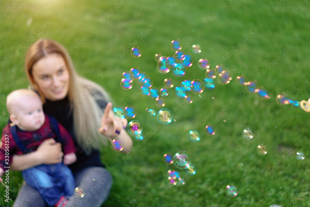 Unfocused unrecognizable mother inflates soap bubbles with her little son in a park on a sunny summer day. focus on the bubbles Unfocused unrecognizable mother inflates soap bubbles with her little son in a park on a sunny summer day. focus on the bubbles