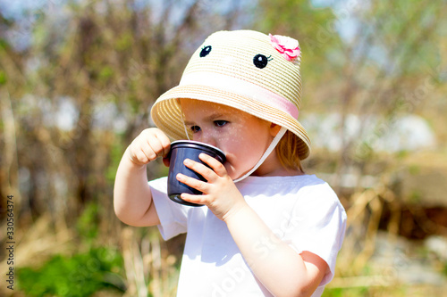 Child drinks water from a plastic cup  in the spring garden, holds a plastic cup in his hands