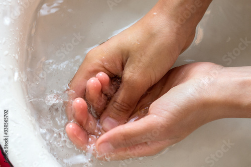 Child’s hands under white bowl with water upon water stream, colorful soaps on a white material, cleanliness and hygiene concept 