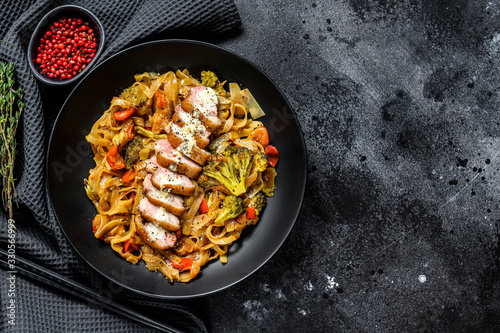 Wok noodles with duck meat and vegetables. Black background. Top view. Copy space