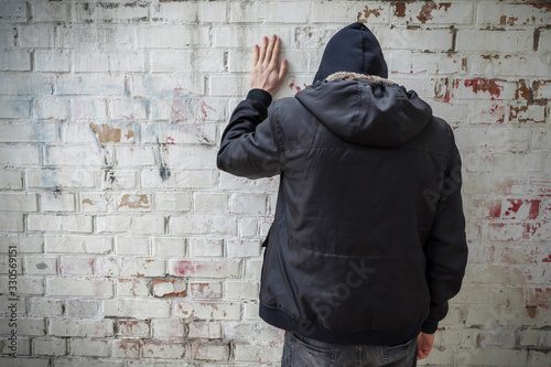 A man in a hood experiencing a crisis of dependence against a brick wall. The view from the back. Addiction concept.