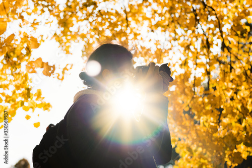 Photographer silhouette shooting autumn leaves in park outdoor. Bright sun flare comming thrugh photo