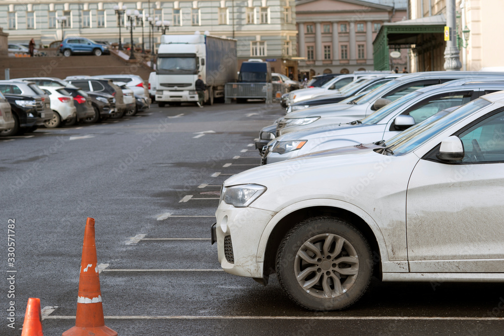 A row of cars parked in the Parking lot against the background of city buildings. Background