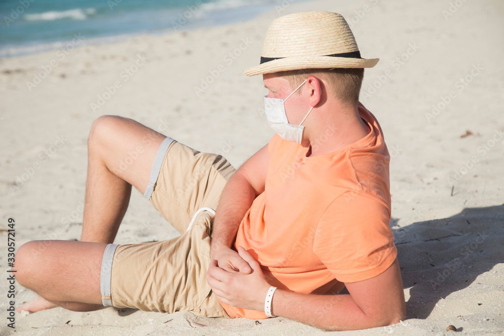 a man with a medical protective mask for coronavirus on the beach in a tropical country at summer sunny day