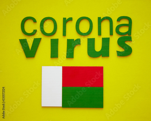Flag of Madagascar And Word CORONAVIRUS made of green cardboard letters, isolated on yellow background.