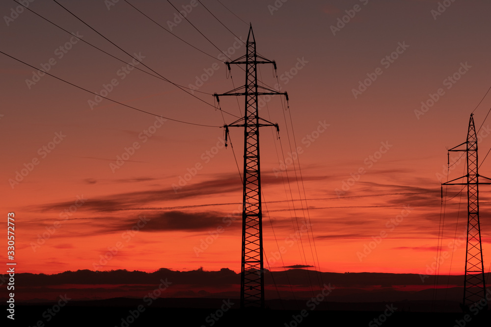 Silhouette of high voltage lines and transmission towers thru the Moravian field at sunrise