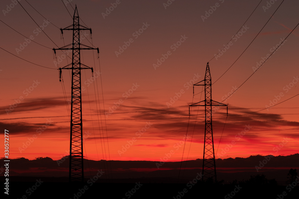 Silhouette of high voltage lines and transmission towers thru the Moravian field at sunrise