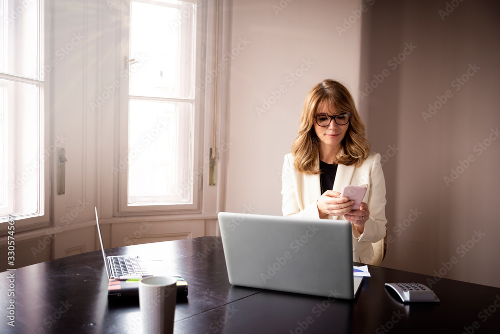 Middle aged woman text messaging and working on laptop at home Middle aged woman text messaging and working on laptop at home