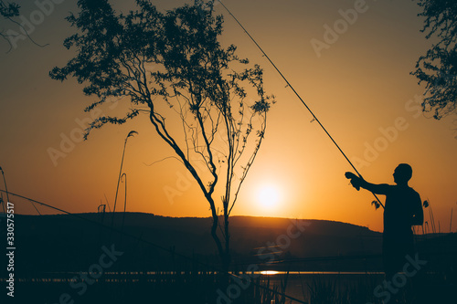Silhouette of a fisherman fishing on a lake at sunset