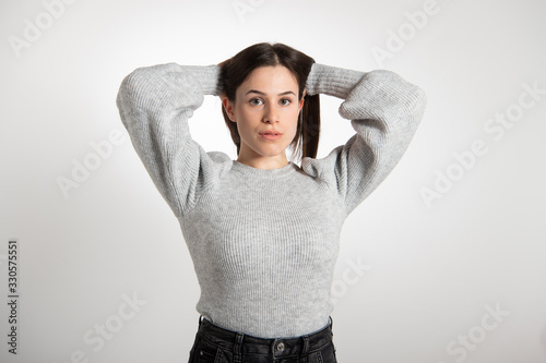 Beautiful girl in big grey sweater with hands behind her head looking at camera. Young pretty woman with perfect makeup and red lipstick...