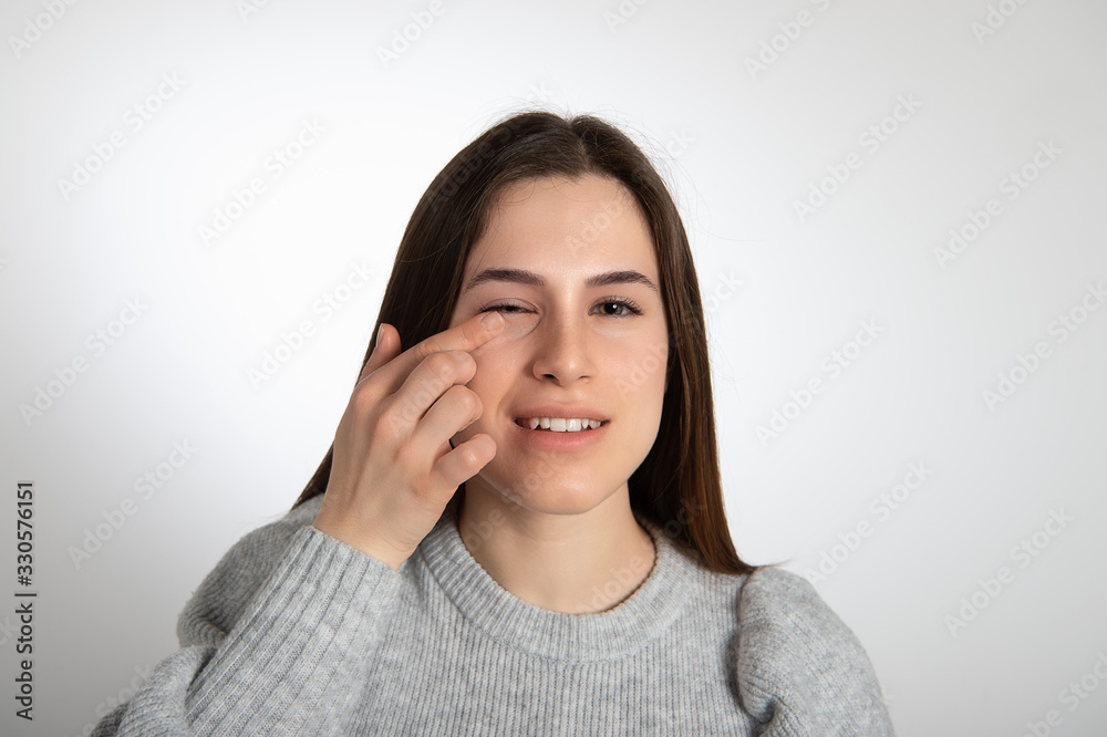 Portrait of young attractive brunette girl with fresh clean skin looking at camera and touching her face with pointing finger. Isolated on white background... Portrait of young attractive brunette girl with fresh clean skin looking at camera and touching her face with pointing finger. Isolated on white background...