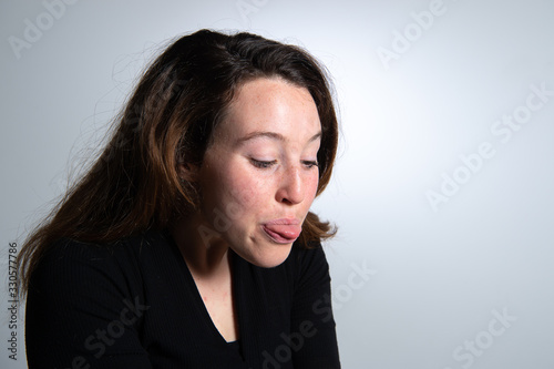 View of cheerful young brunette woman looking to the side over white background. Girl sticking her tongue out. Emotions in female face...