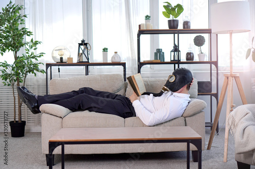 Pandemic coronavirus quarantine period concept. National quarantine concept. A man in a gas mask lies on a sofa and reads a book. Stay at home idea. photo