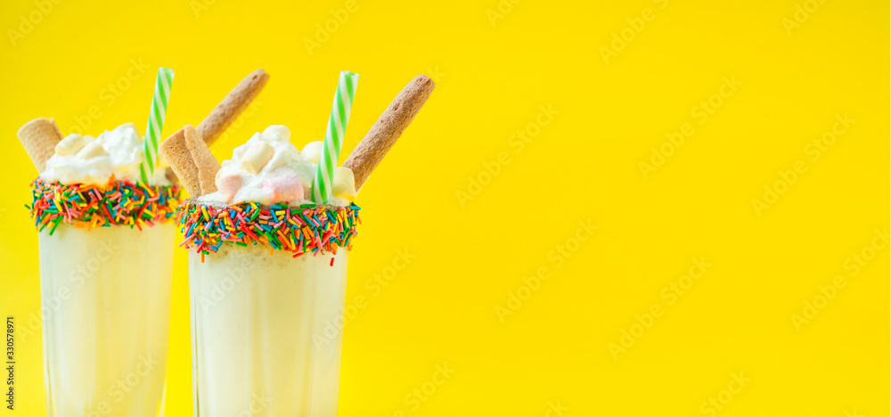 Milkshake with ice cream and whipped cream, marshmallows, waffles, served in a glass cup decorated with pastry dressing. Summer cocktail. Bright yellow background. Banner. Copy space. Milkshake with ice cream and whipped cream, marshmallows, waffles, served in a glass cup decorated with pastry dressing. Summer cocktail. Bright yellow background. Banner. Copy space.