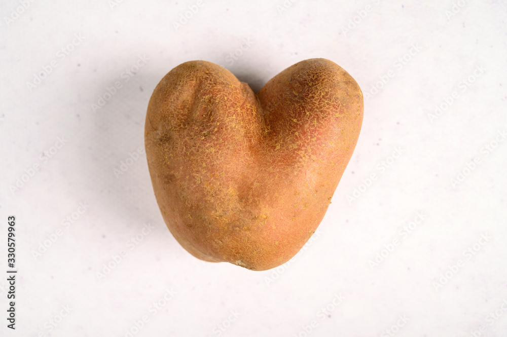 Obraz premium Ugly potato in the shape of a heart on a gray background. Funny, ugly vegetables.
