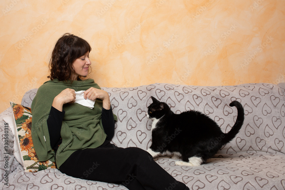 Φωτογραφία Beautiful woman with paper tissue in hands sitting on couch and looking at her black and white cat pet