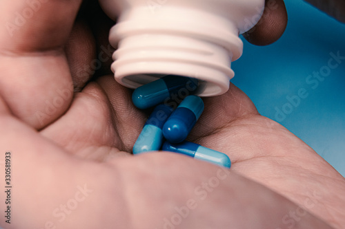 Man s hands with pills   spilling tablets out of pill bottle on a blue background.