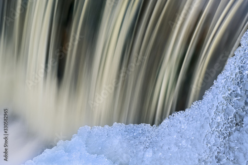 Winter landscape of the Battle Creek River Cascade captured with motion blur and framed by icicles, Michigan, USA