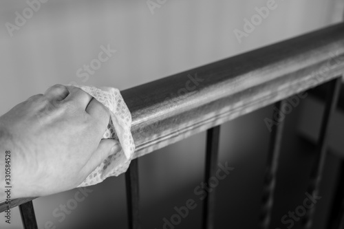 Caucasian hand with disinfecting wipe used for sanitizing a wooden stair railing