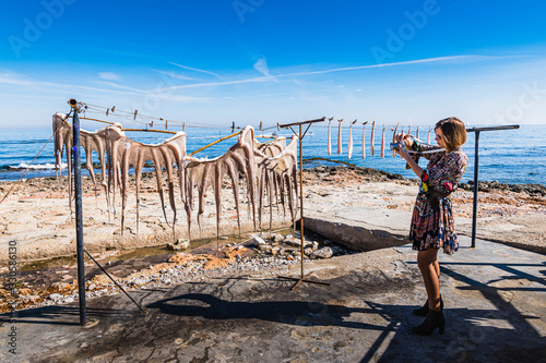 Фотография Tourist girl photographing the sun-dried octopus, one of the gastronomic delicac