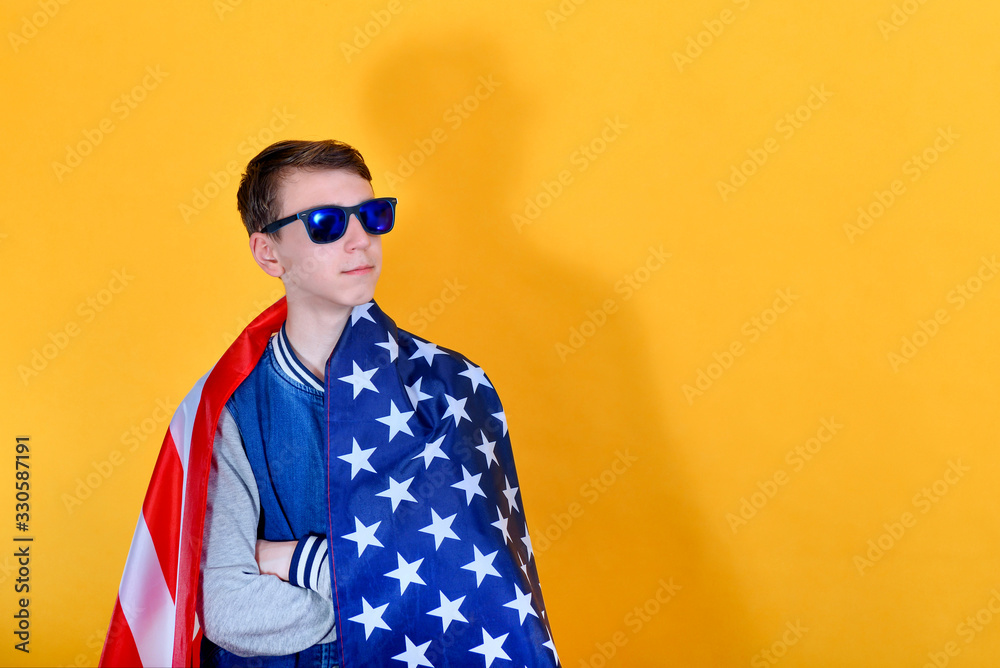 Teenager teenager in sunglasses with an American flag on his shoulders looks away, the concept of confidence in the future. Teenager teenager in sunglasses with an American flag on his shoulders looks away, the concept of confidence in the future.