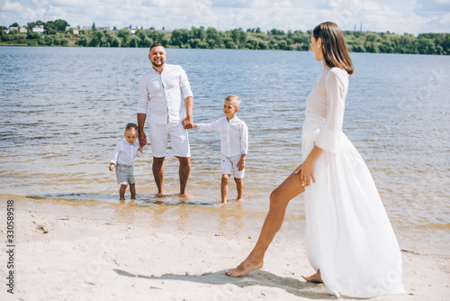 Young family with kids in white clothes walking on the sandy beach, they have fun. © Олег Кошевський