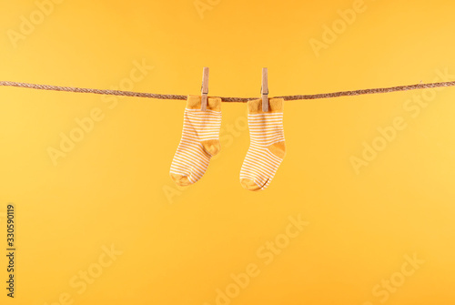 Baby socks hanging on rope against color background