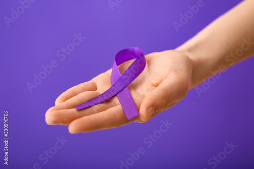 Female hand with violet ribbon on color background. Domestic violence concept