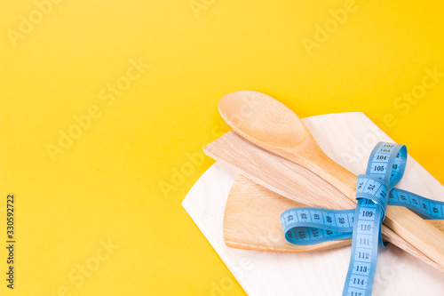 cutting board and wooden kitchen appliances tied up with a blue measuring tape bow, yellow background, copy space, diet concept, eco friendly life style