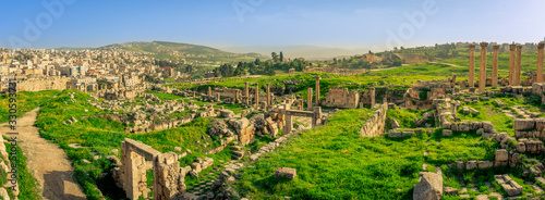 Panorama overview of the Roman site of Gerasa, Jerash, Jordan, with ruins, pillars and remains of the old city clearly visible. Green grass and blue sky on a sunny day in spring. 