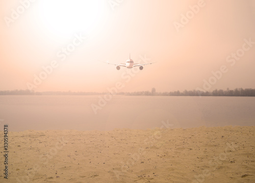 Airplane over the lake in the orange sky with the sun. Nature and transport